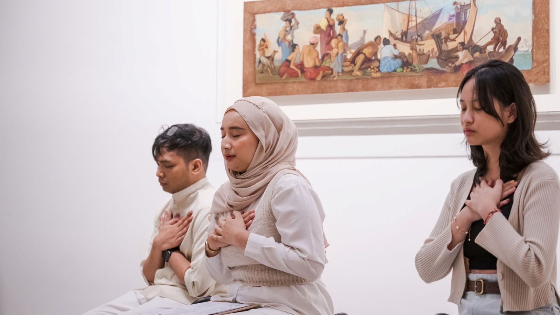 A trio of people sitting in chairs, each with their hands clasped, indicating a moment of contemplation or mindfulness.