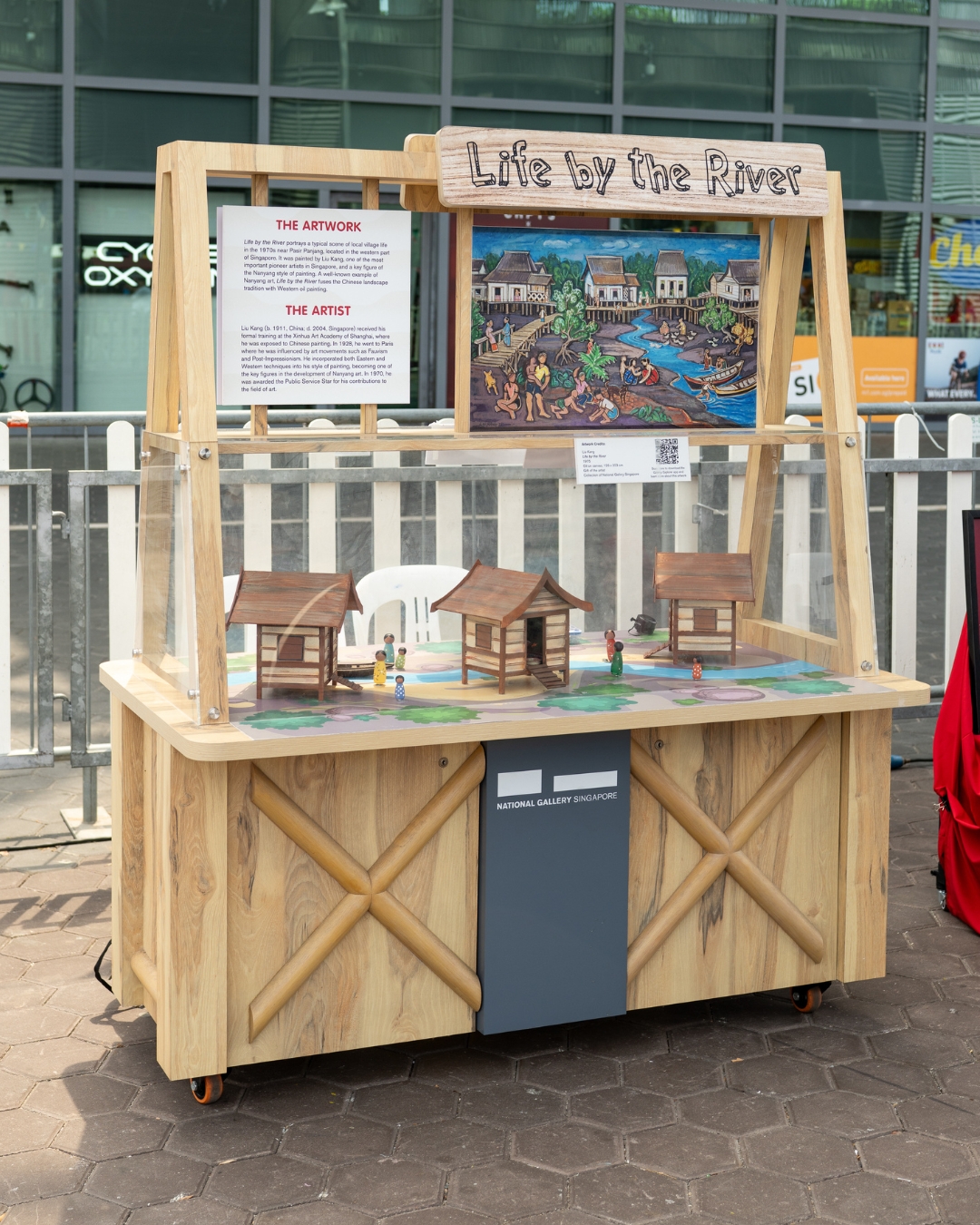 A wooden display case showcasing an interactive art project inspired by Liu Kang's 'Life by the River.'