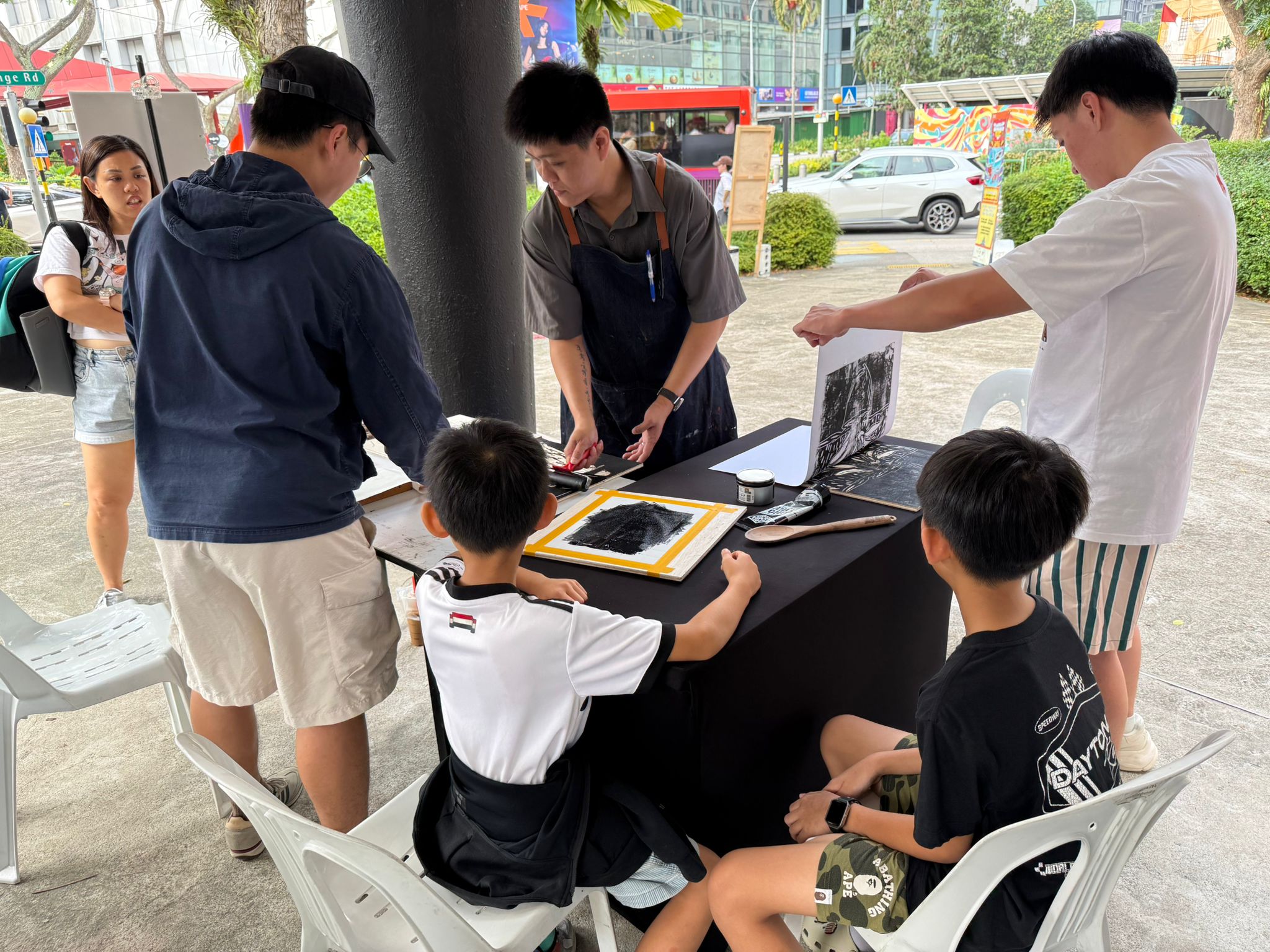A group of people engaged in art activities at a table, exploring batik painting and woodblock printing techniques.