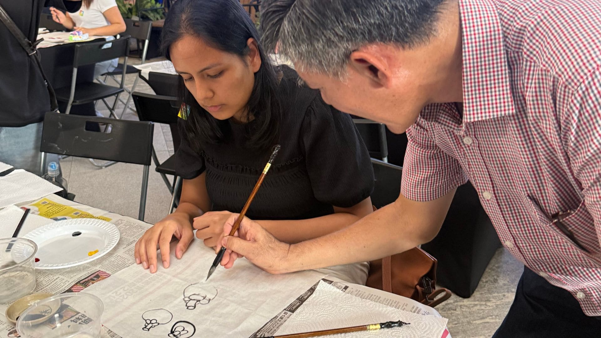 A man and woman engaged in drawing on paper, showcasing their creativity and teamwork in a bright setting.