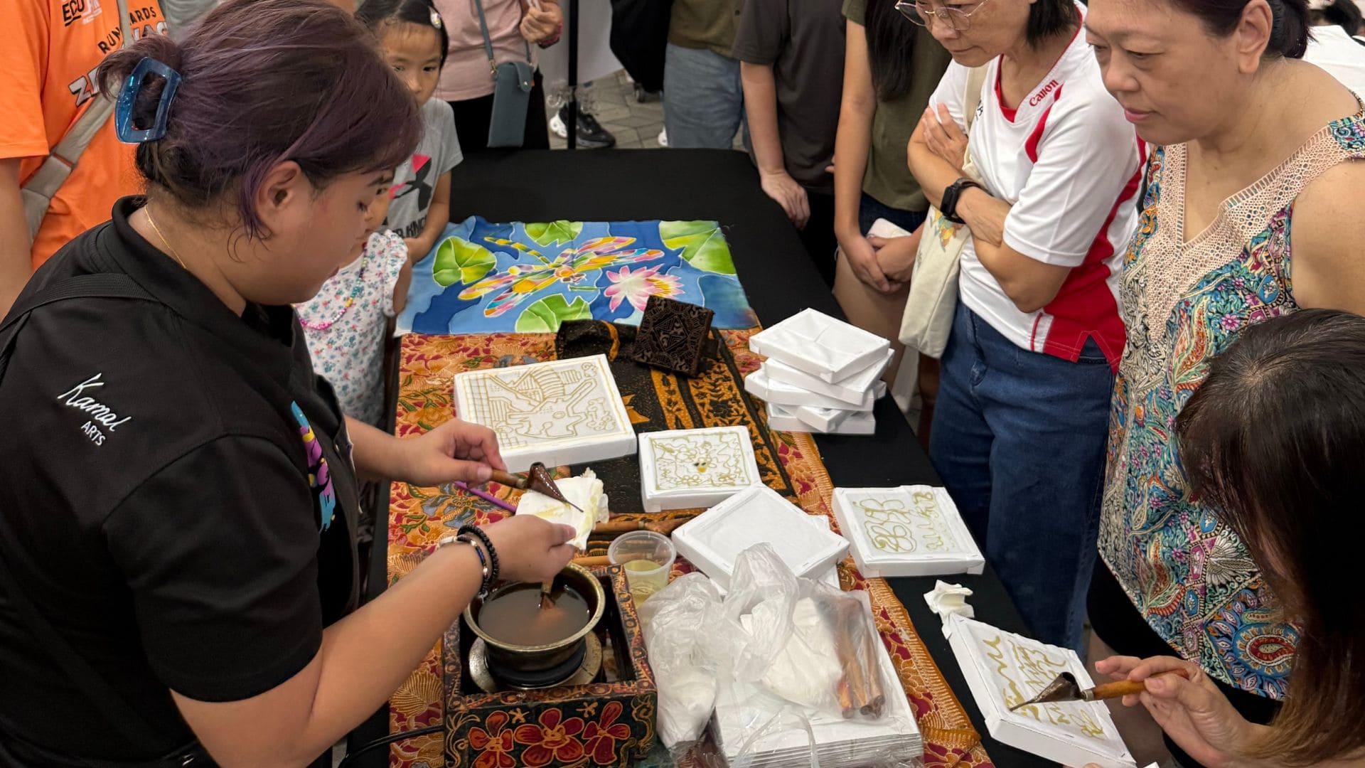 A group of people gathered around a table, engaging with batik during an art workshop.
