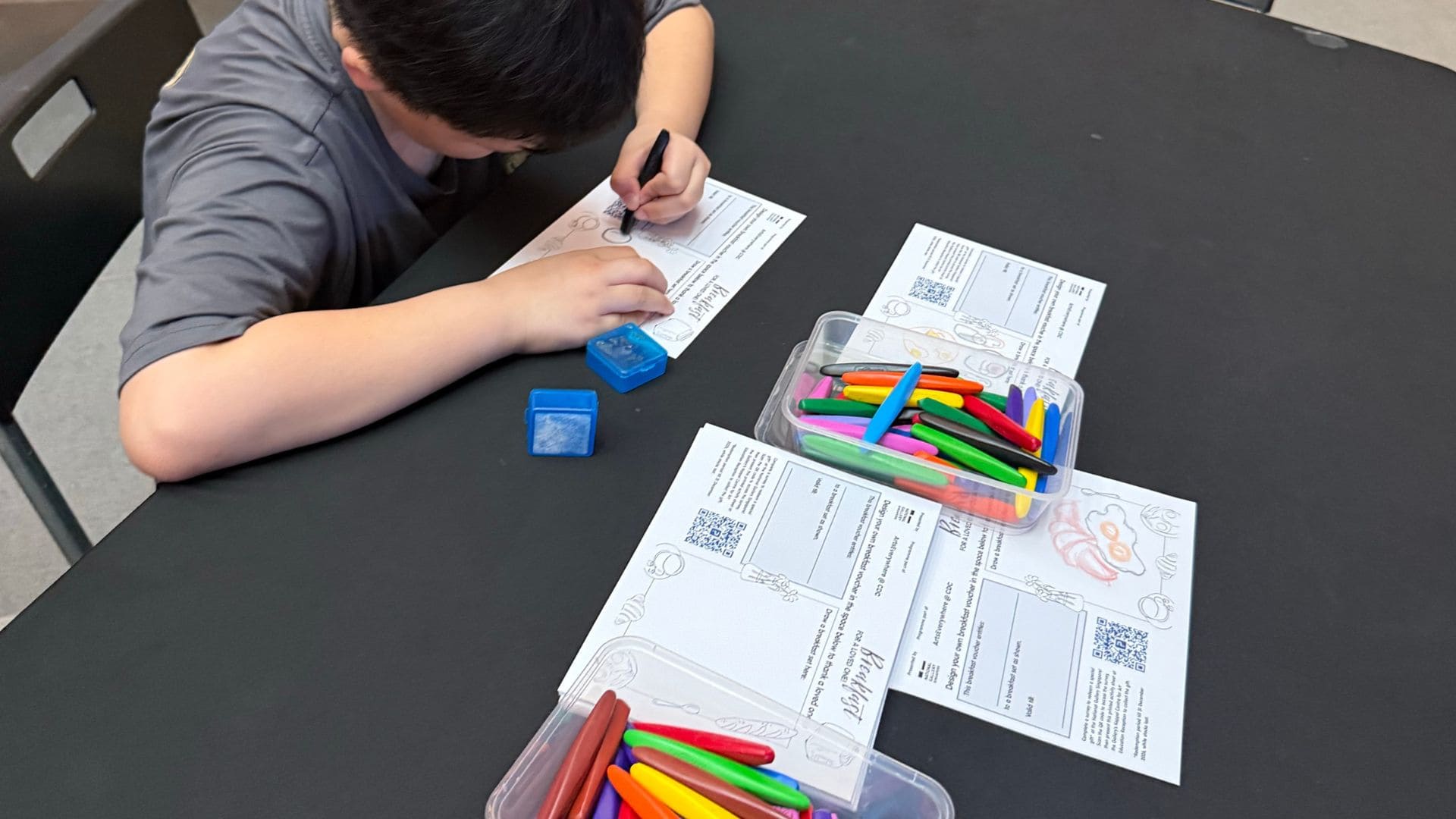 A young boy focused on writing with colorful markers on a sheet of paper.