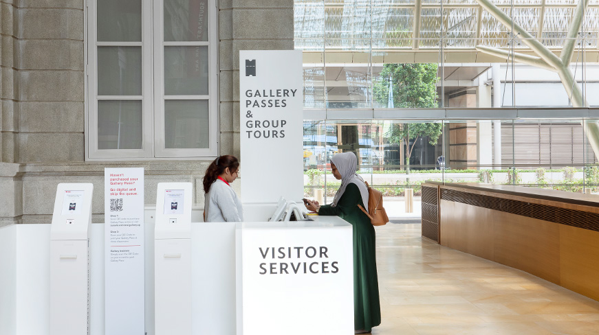 A front-of-house staff member at the Visitor Services counter assists a guest at the Padang Atrium