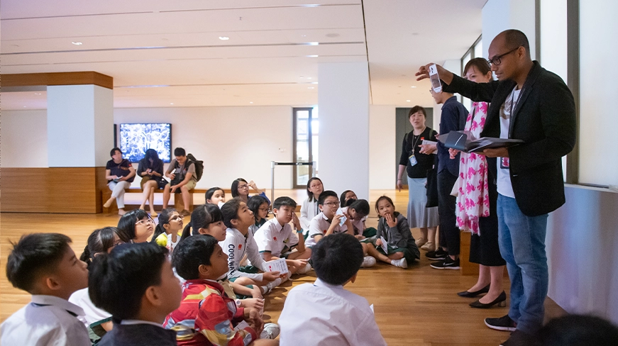 An educator holds up a colour wheel, asking questions to a small group of seated children