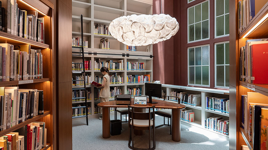 A visitor browses a well-lit library room filled with bookshelves and archival materials