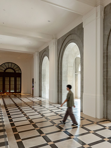 A man walks across the tiles of the empty former Supreme Court Foyer, with sunlight streaming in through the arched doorways