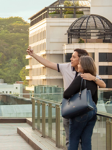 Side view of a couple taking a selfie on the Coleman Deck in the late afternoon sun, with buildings in the background