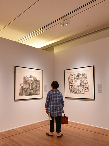 Back view of an old lady staring at two Chinese ink paintings on the wall in an exhibition gallery space