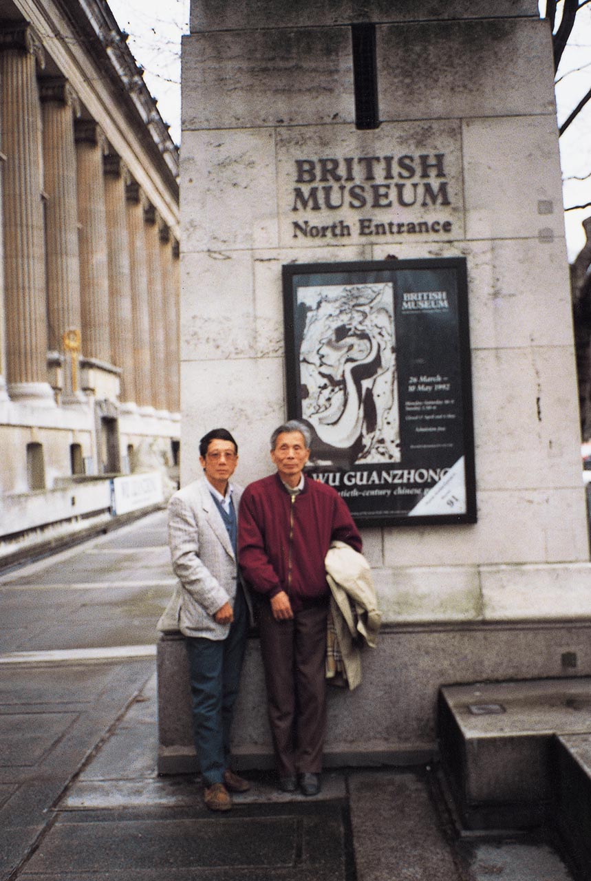 Photograph of Wu Guanzhong and his son, Wu Keyu before the poster of Wu's exhibition titled "Wu Guanzhong: a twentieth-century Chinese painter"