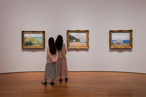 Two people viewing Monet paintings on a white wall