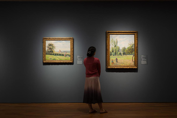 Person viewing Impressionist painting on display within exhibition space