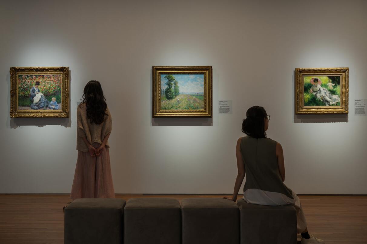 People viewing Impressionist artworks on display in dim light