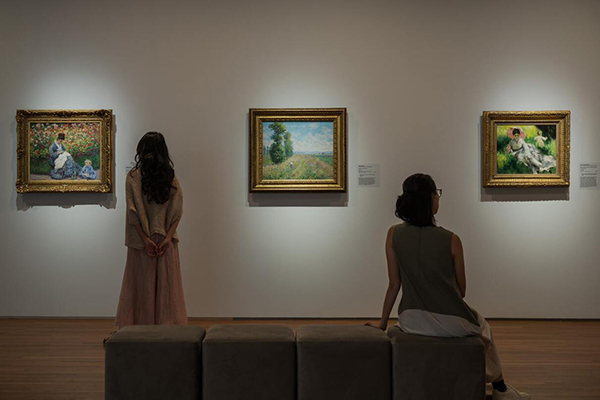 People viewing Impressionist artworks on display in dim light