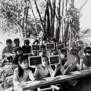 Guerilla Students from Kinh Hàng Hamlet, Khánh Hưng Commune, Trần Văn Thời District, Cà Mau, Seated on Makeshift Wooden Boards which are Later Removed Once Class is Over, Leaving No Traces Behind