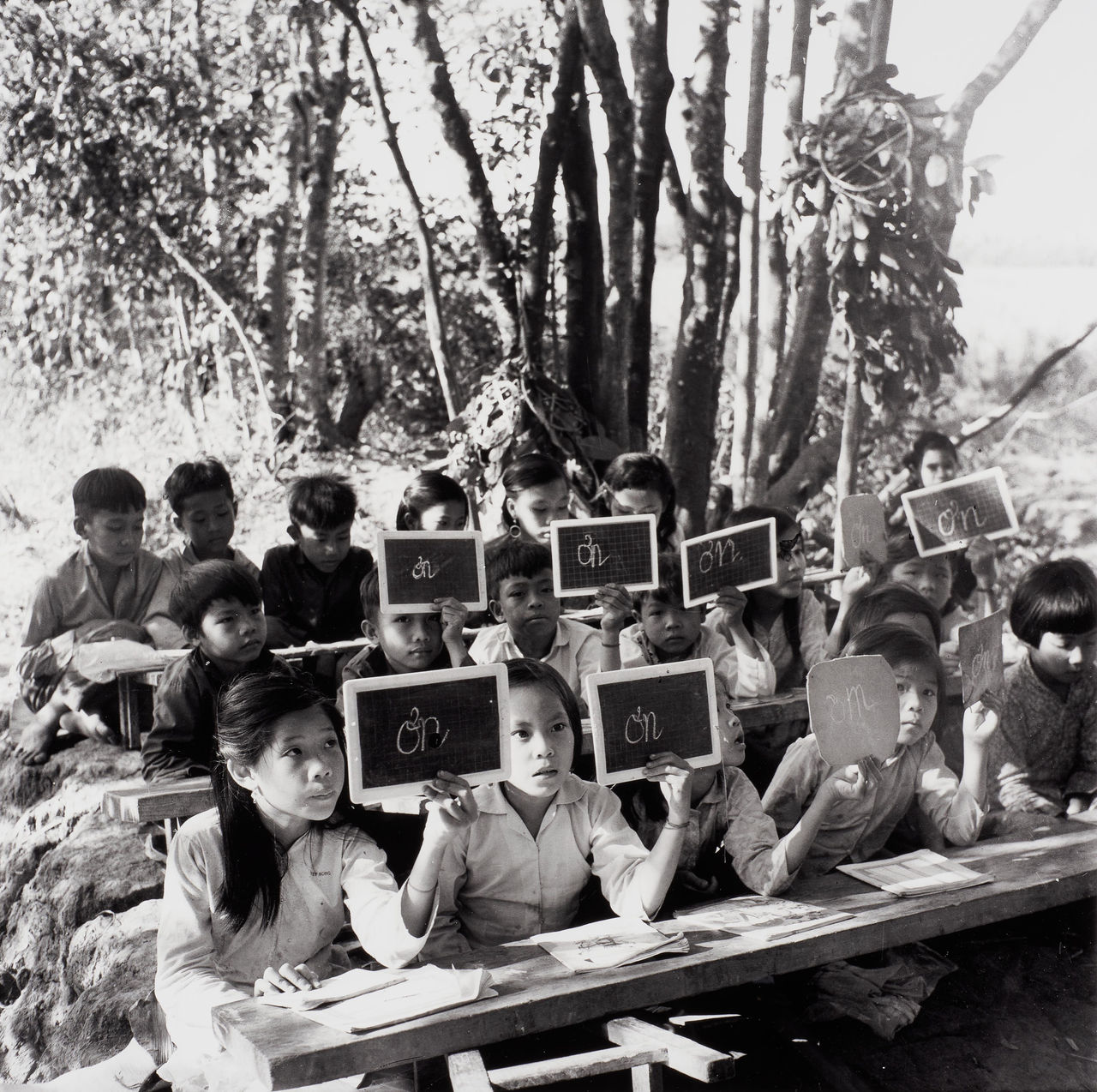 Guerilla Students from Kinh Hàng Hamlet, Khánh Hưng Commune, Trần Văn Thời District, Cà Mau, Seated on Makeshift Wooden Boards which are Later Removed Once Class is Over, Leaving No Traces Behind