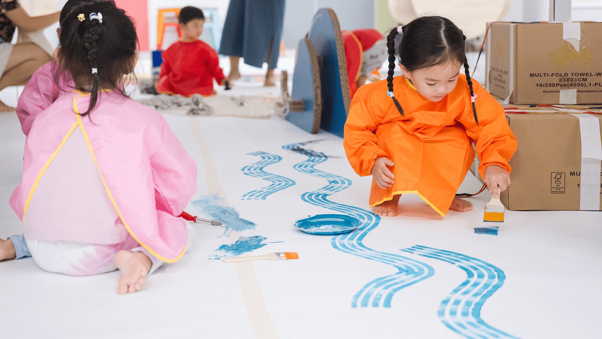 Children holding paintbrushes and painting a bit mural on the floor