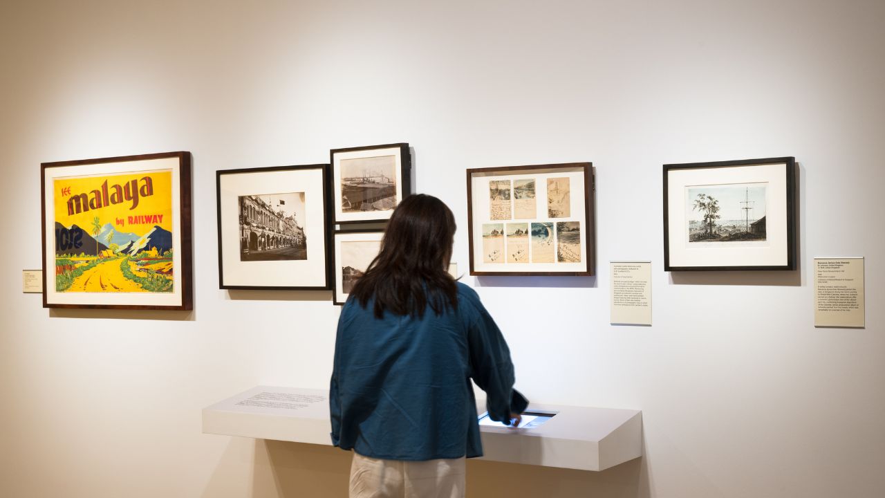 Visitor interacting with exhibition materials in a gallery, with artworks hung on white walls.