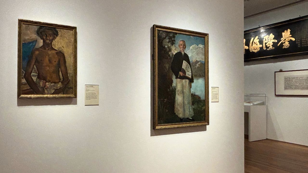 Gallery displaying two portraits on white walls; left shows a shirtless man, right depicts a man holding a fan. Calligraphy art in the background.