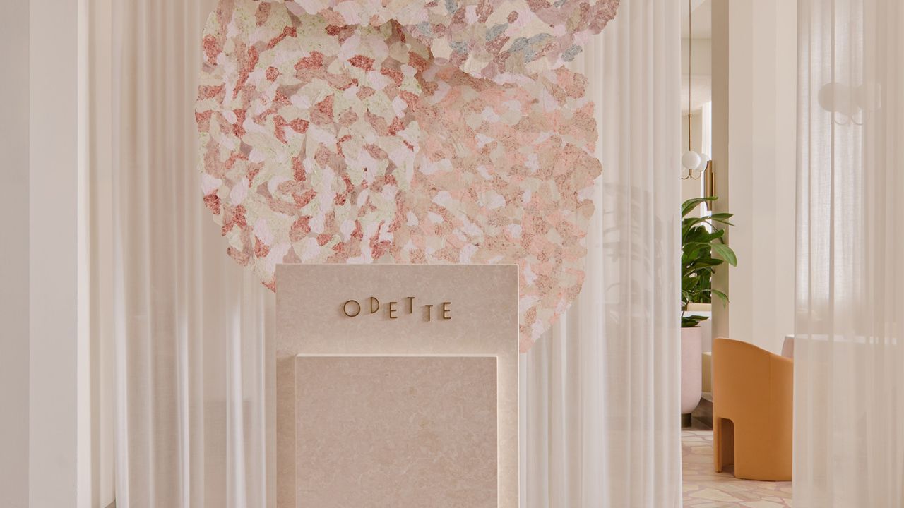 The elegant hostess stand at Odette, a three-Michelin-star French restaurant in Singapore, sits beneath a suspended floral-inspired art installation. Soft drapery, warm neutral tones and refined furnishings create a welcoming and sophisticated entrance.
