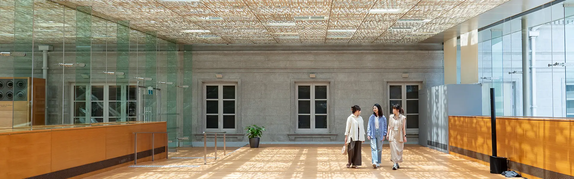 Three women happily chatting and walking through a grand art gallery information centre with concrete walls and a patterned roof screen
