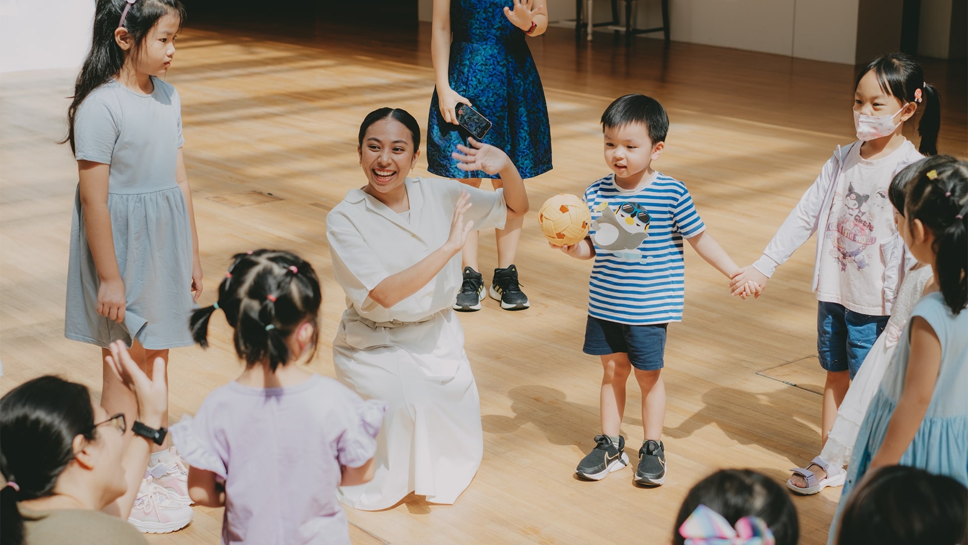 Group of children and parents taking part in an expressive movement activity inside a brightly lit gallery as the facilitators guide them