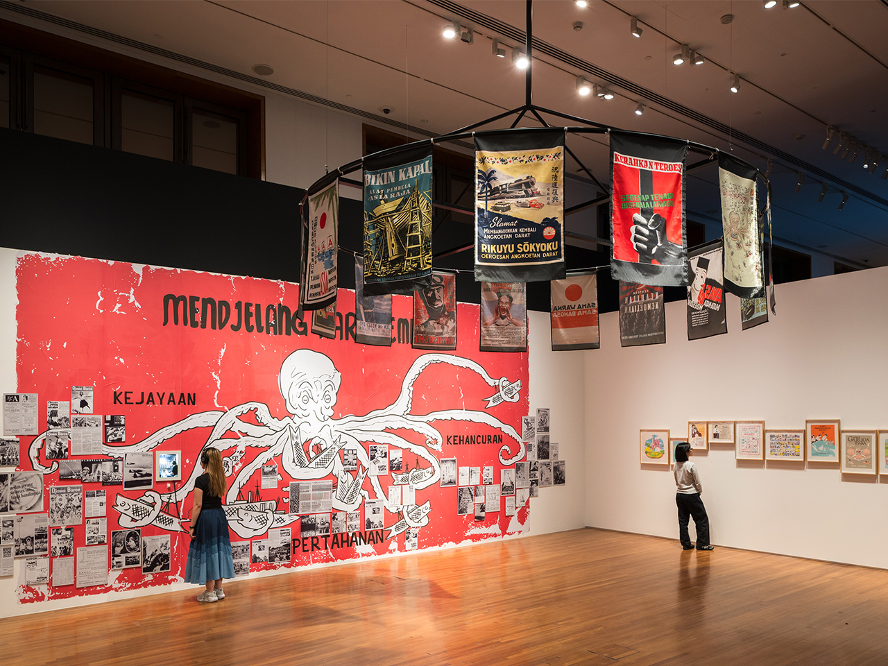 Exhibition view of "Art Remembers" at National Gallery Singapore, showcasing artworks on red walls and banners beneath a chandelier.