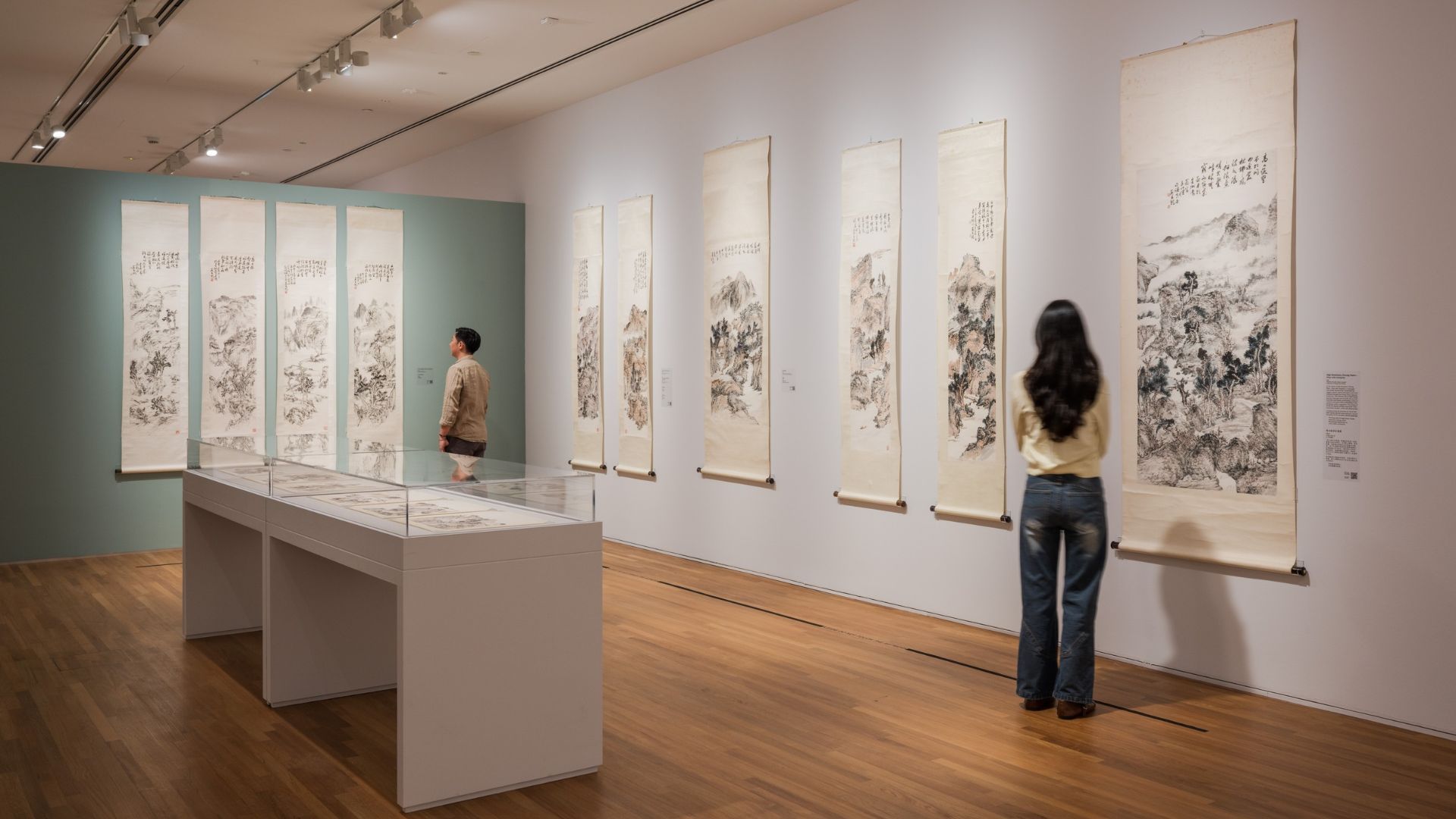 Two visitors observe a Chinese artwork by Fan Chang Tien in a museum setting, surrounded by other art pieces.