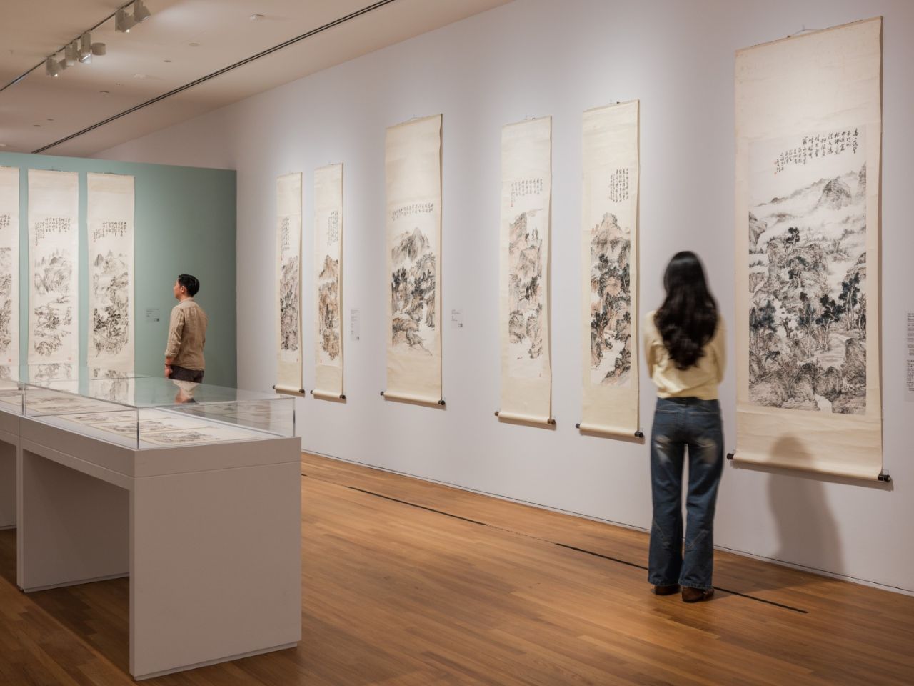 Two visitors observe a Chinese artwork by Fan Chang Tien in a museum setting, surrounded by other art pieces.