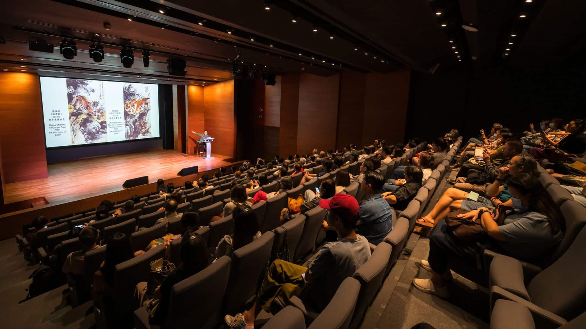 A large auditorium filled with people seated in rows of chairs, engaged in an event or presentation.