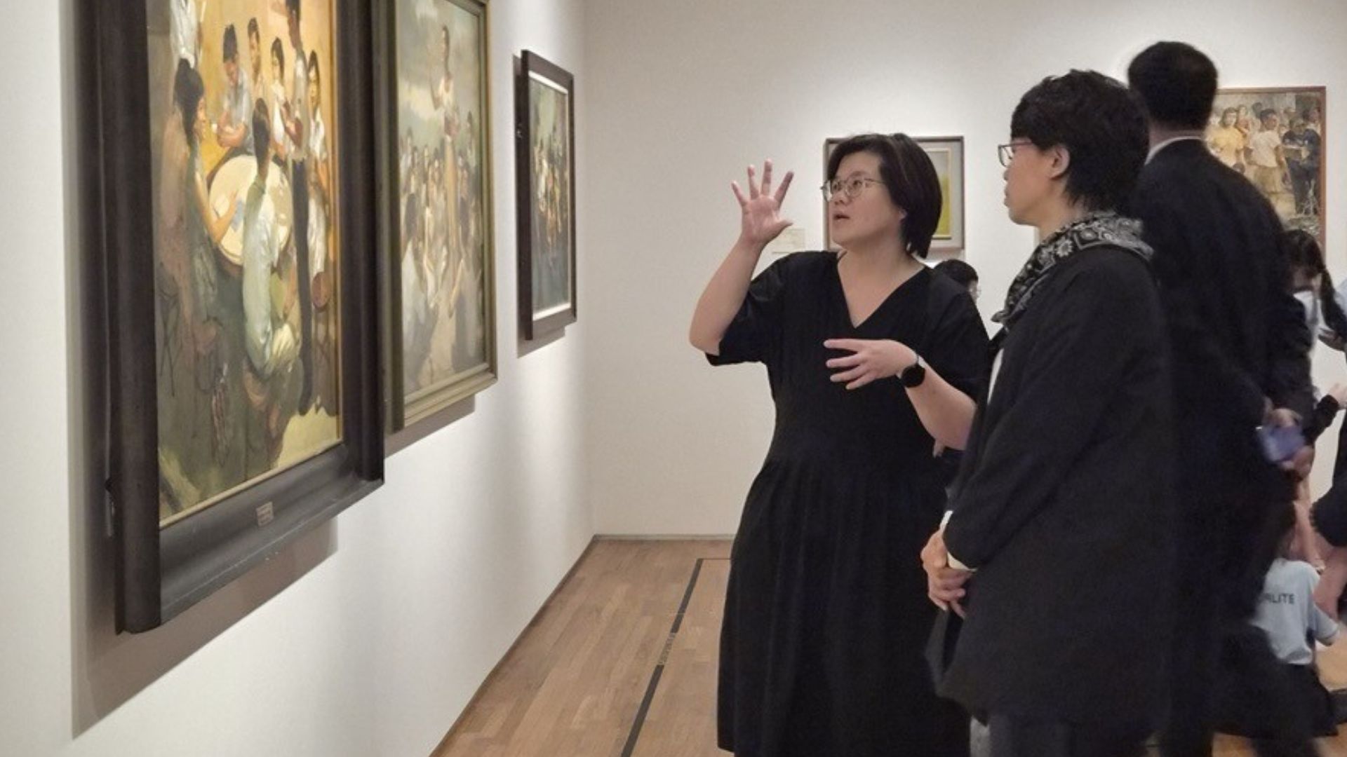 A museum visitor stands before three horizontal artworks admiring them. The artworks featuring photographed scenes, with a description mounted on white card next to each respective work.