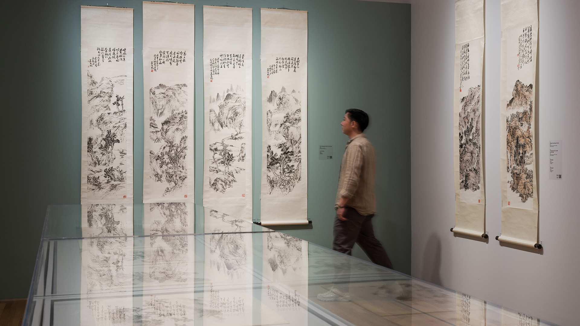 A man observes various Chinese ink paintings displayed in an art museum, engaged in the artistic experience.