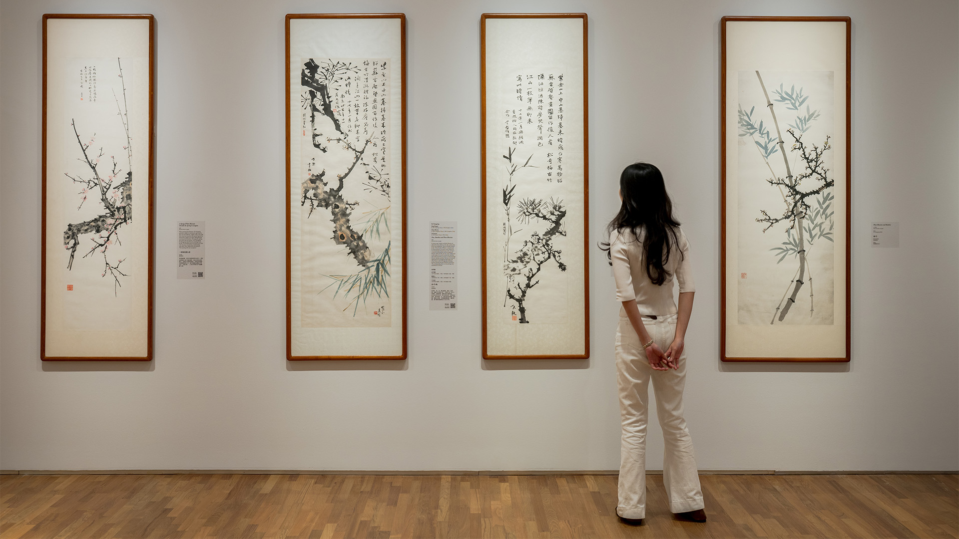 A woman examines artwork on display in an art museum, appreciating the creativity and detail of the Chinese ink paintings.