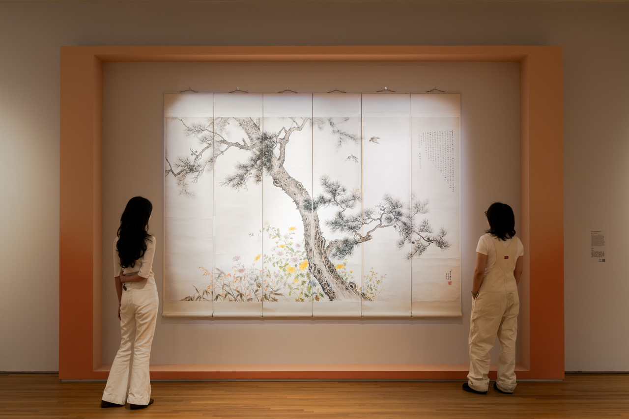 Two women stand in front of a wall, examining a Chinese ink painting together.
