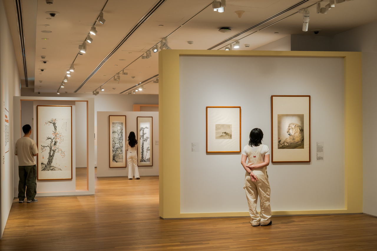 Three people stand in an art gallery, thoughtfully examining the Chinese ink paintings on the walls.