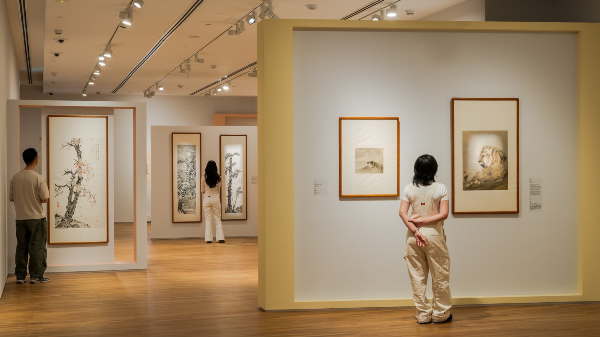 A woman observes various paintings displayed in an art gallery, engaged in the Chinese paintings around her.