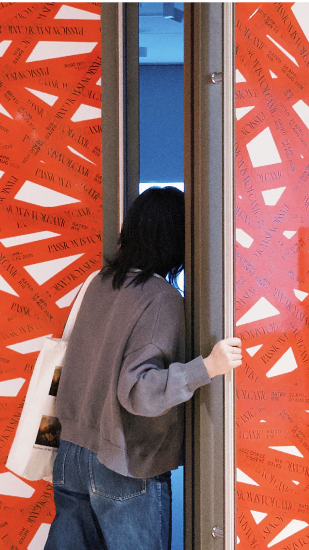 A woman looks through a door with red tape, into the Passion is Volcanic: Desire in Southeast Asian Art exhibition
