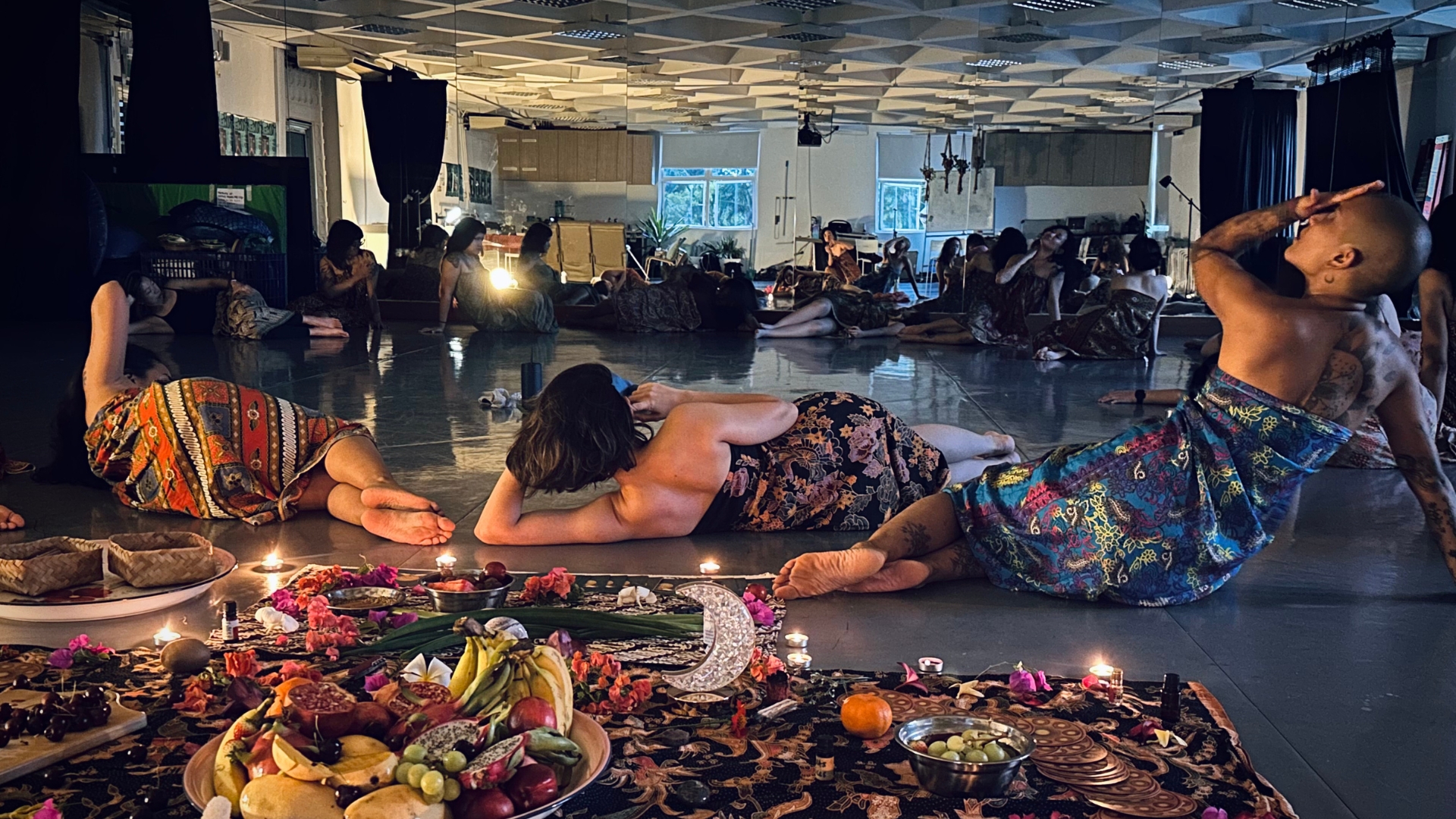 A diverse group of people sitting on the floor, sharing food and surrounded by flickering candles, enhancing the ambiance.