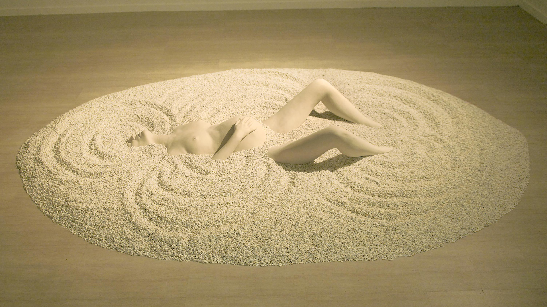 Exhibition installation image that features the sculptural installation, Haliya Bathing, which depicts a pregnant female figure sinking into sand.