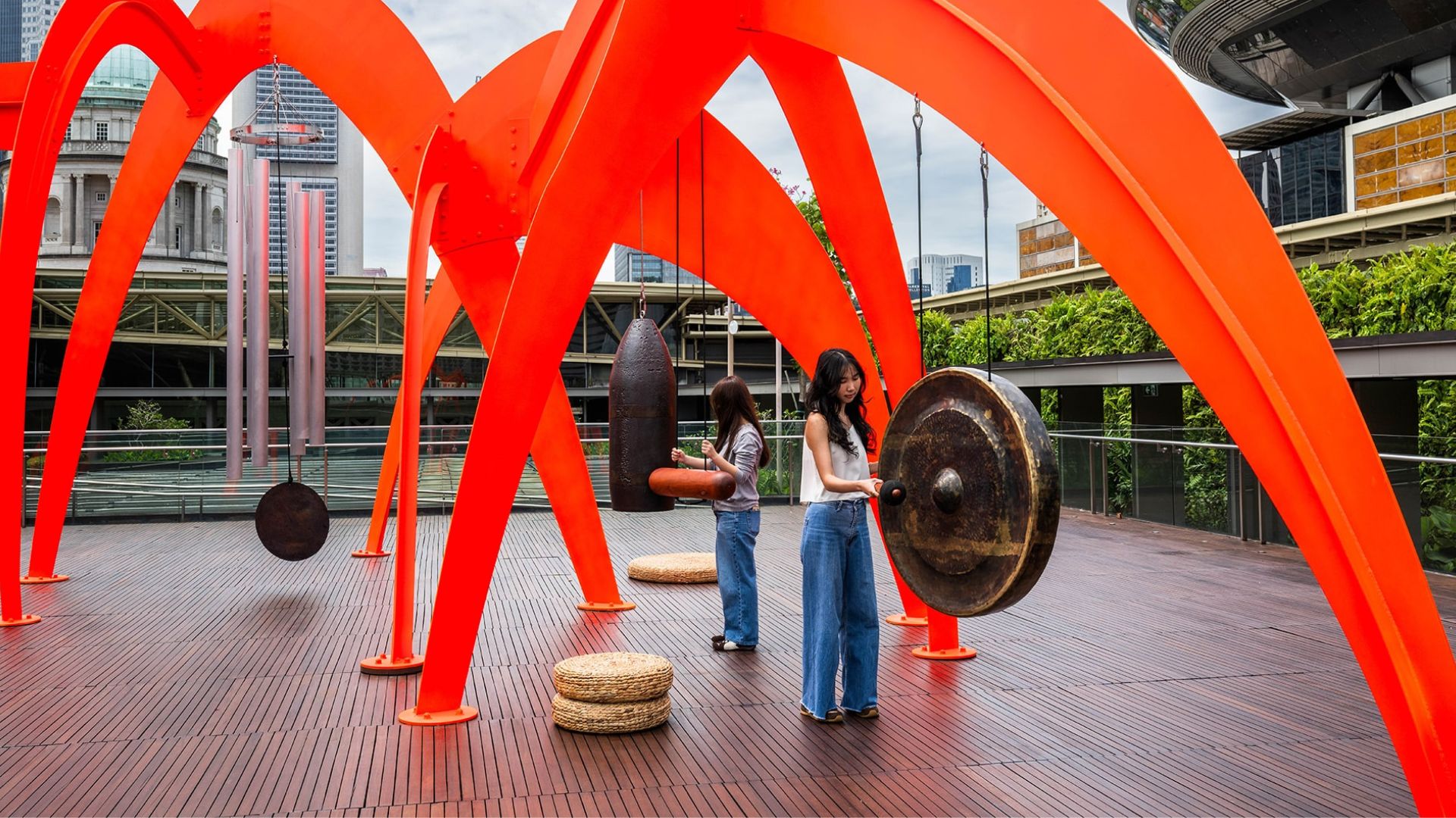Two women are standing next to a large orange sculpture, enjoying the artistic display in an outdoor setting.