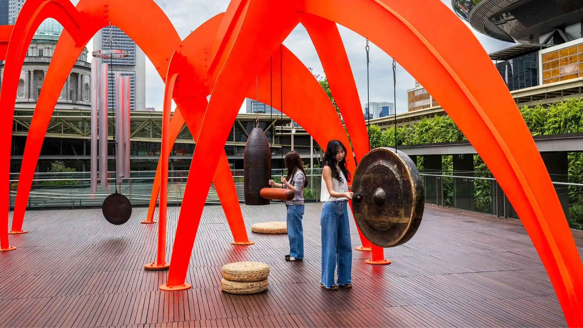 Two women are standing next to a large orange sculpture, enjoying the artistic display in an outdoor setting.