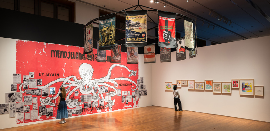 Exhibition view of "Art Remembers" at National Gallery Singapore, showcasing artworks on red walls and banners beneath a chandelier.