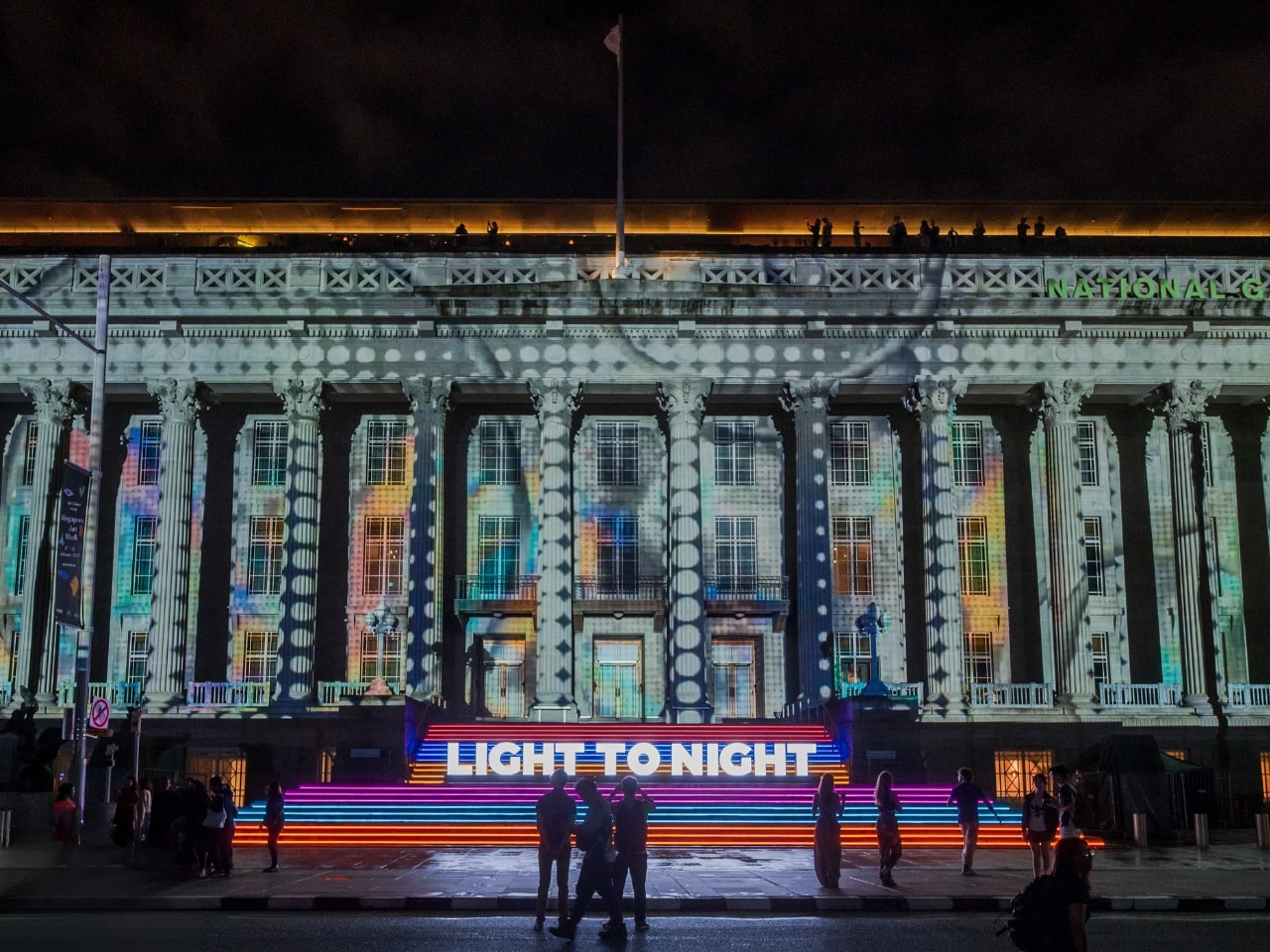 Nighttime scene of classical building illuminated with colorful light projections during Light to Night festival