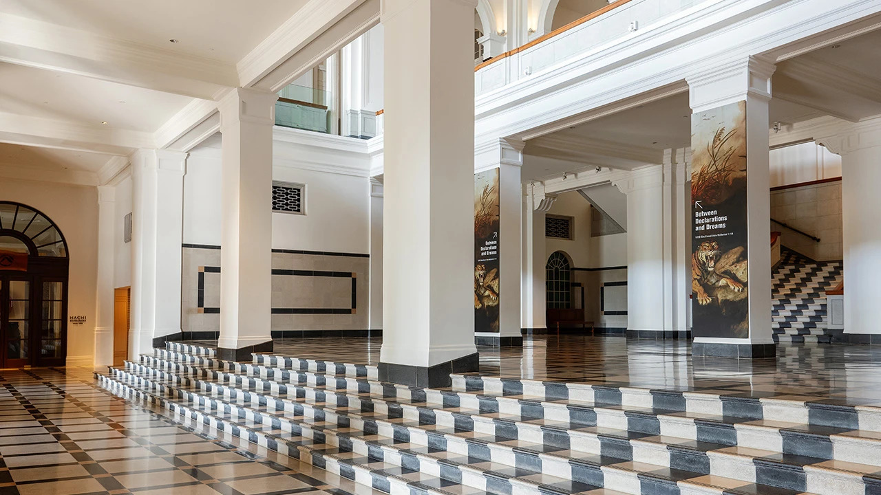 Exhibition banner for Building Highlights- Interior view of the National Gallery Singapore’s historic building with grand white columns and patterned marble steps, featured in the Building Highlights guided tour.