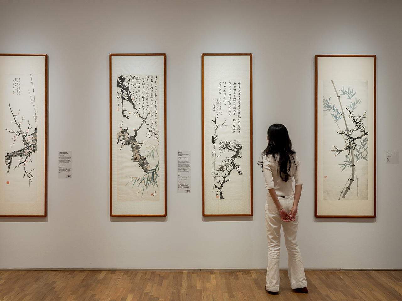A woman examines artwork on display in an art museum, appreciating the creativity and detail of the Chinese ink paintings.