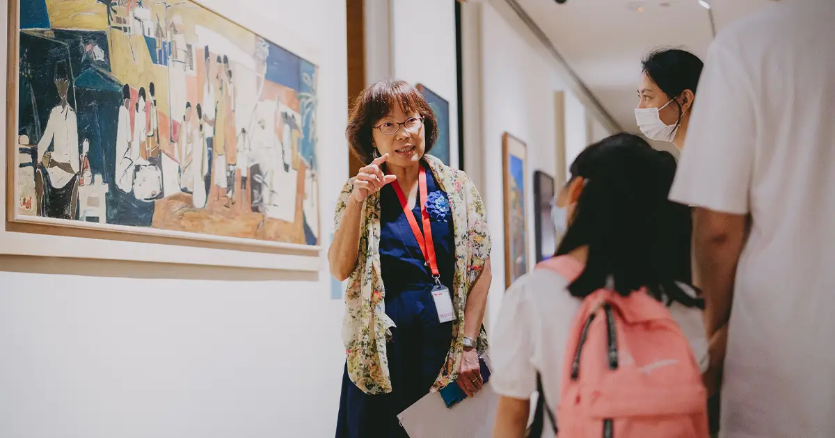 A woman and a child discuss a painting, surrounded by a few other visitors in an art gallery.