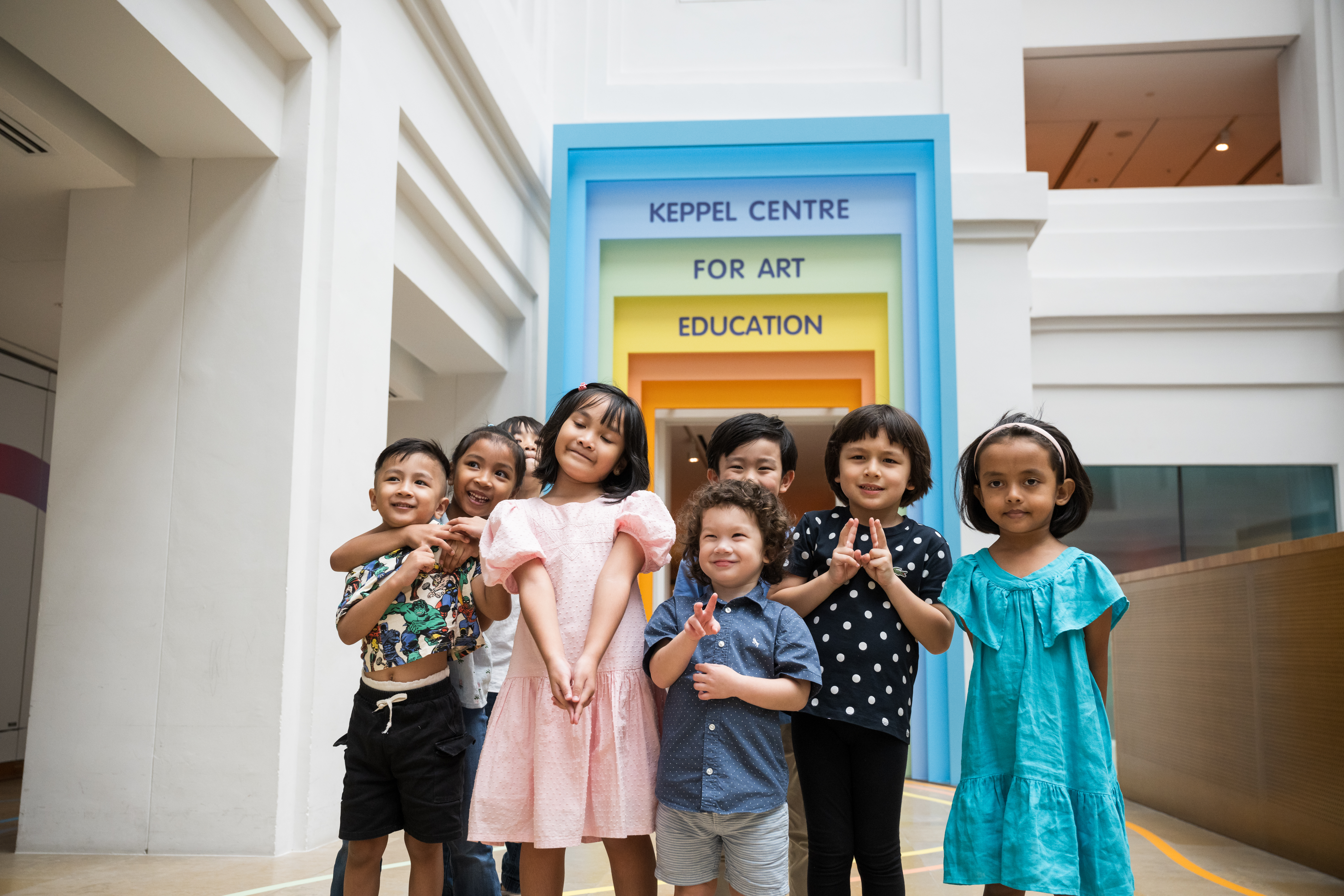 Group of children posing in front of the colorful entrance to Keppel Centre for Art Education in an indoor space