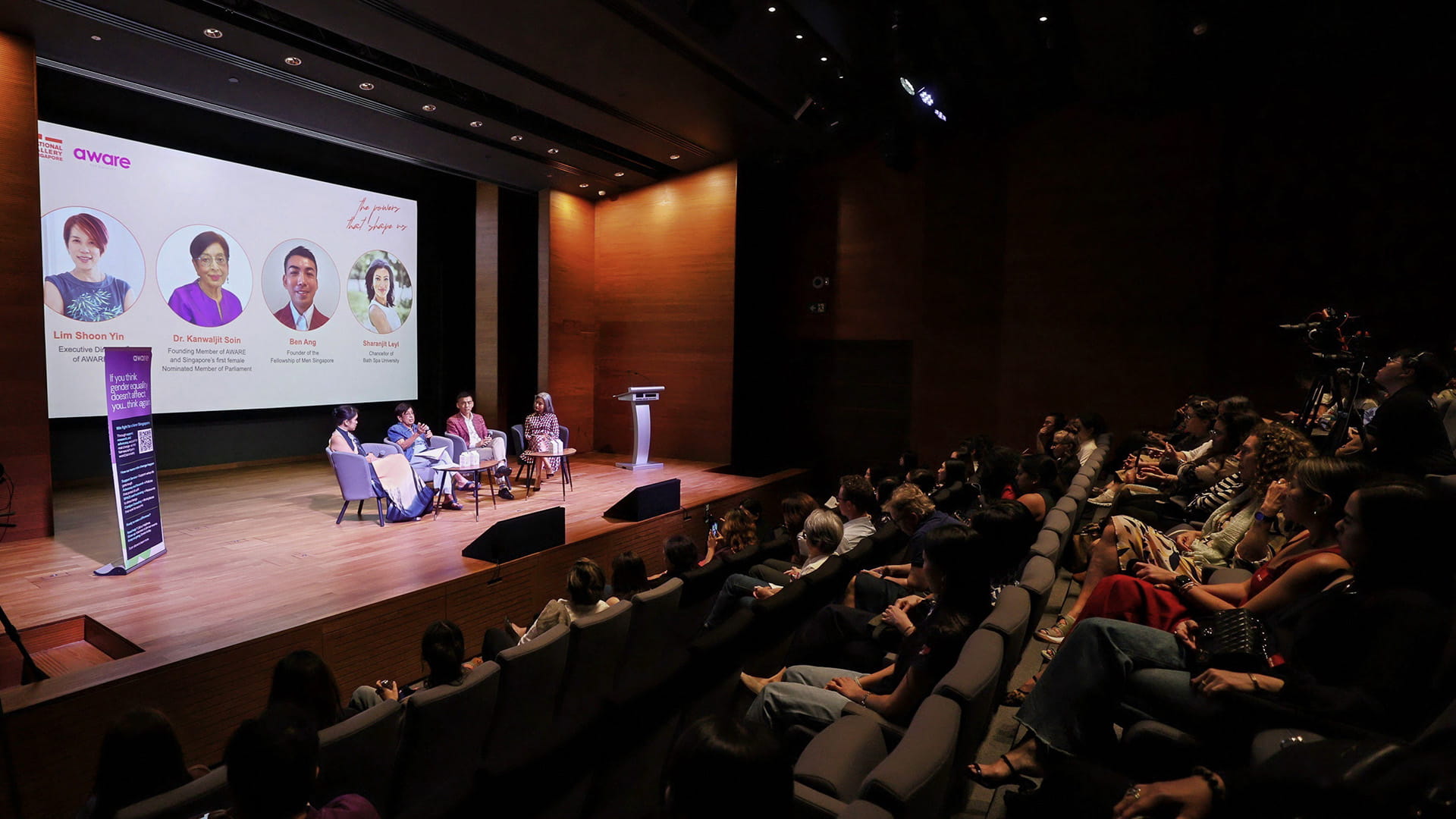 A diverse group of people seated in an auditorium, attentively watching a panel discussion on memory and body reclamation.