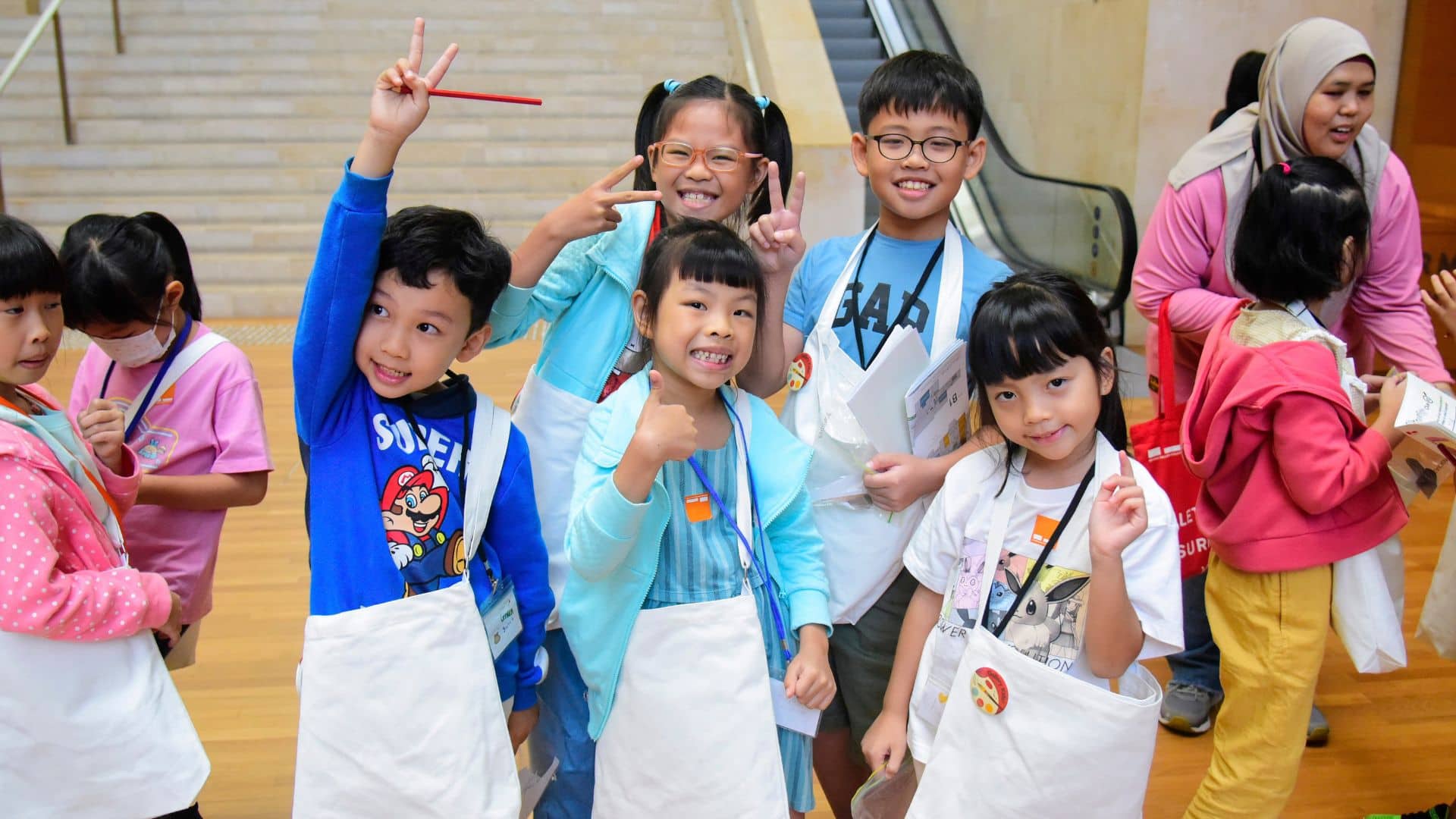 Several children wearing aprons enthusiastically lift their hands, indicating participation in a fun, hands-on learning experience.