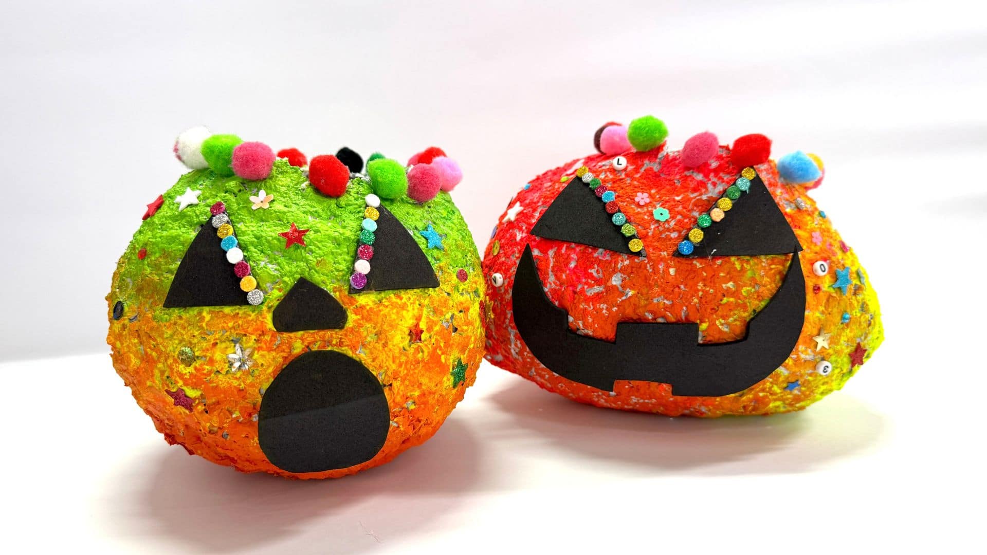Two colorful Halloween pumpkins featuring distinct carved faces, showcasing a cheerful and a spooky expression.